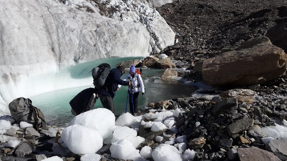 Two trekkers beside a glacial meltwater pool and blocks of ice below the snout of the Haramosh glacier