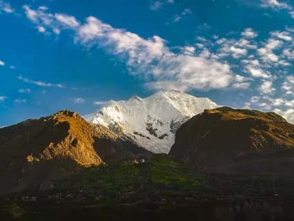 The snow-covered summit of Rakaposhi lit at dusk above green terraced slopes and forest