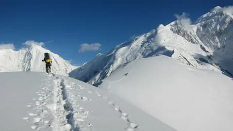 Trekker with a yellow pack following a boot-packed trail across a high snowfield
