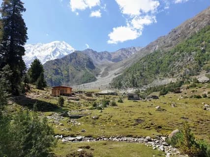 Grassy valley floor with a wooden hut and a rocky stream, a snow-covered peak standing at the head of the valley