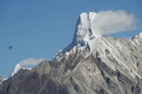 A snow-covered rock spire rising through cloud against a deep blue sky