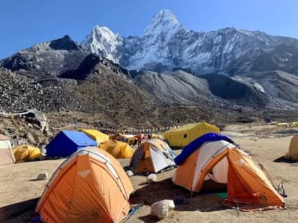 Orange and blue tents on stony ground beneath the snow-covered spire of Laila Peak