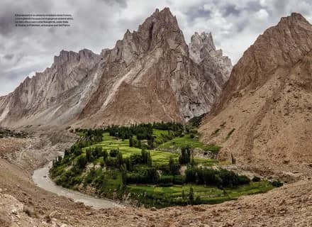 Brown rock spires towering above the green irrigated fields and trees of a Baltistan valley