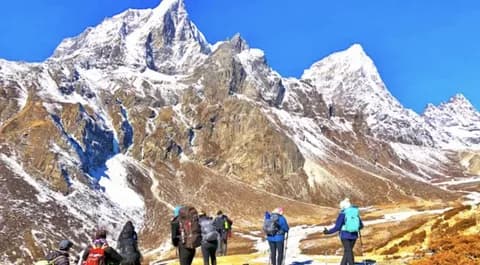 Trekkers with backpacks walking up a rocky path towards the snow-covered Haramosh peaks