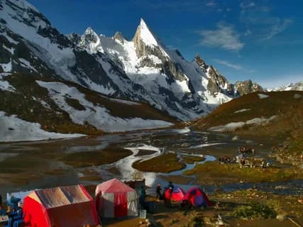 Red and white tents on a braided river meadow with the sharp snow pyramid of Laila Peak above