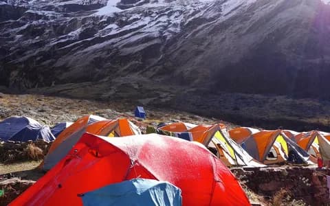 A large camp of red and yellow dome tents spread over a rocky slope below a snow-streaked mountain