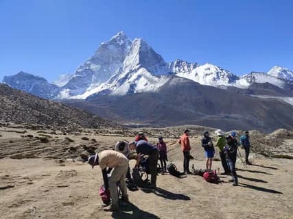 Trekkers sorting gear on a sandy plain with the snow-covered pyramid of Masherbrum towering behind