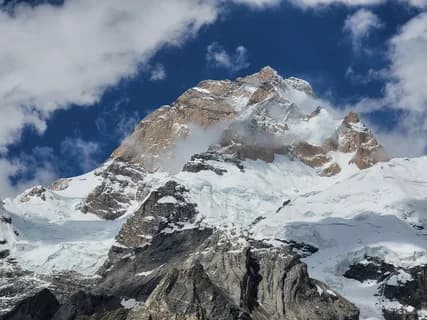 Snow and rock ridges of the Masherbrum upper face rising into cloud against a blue sky