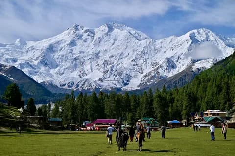 Horsemen and walkers on the Fairy Meadows green with the white wall of Nanga Parbat, pine forest and wooden huts behind