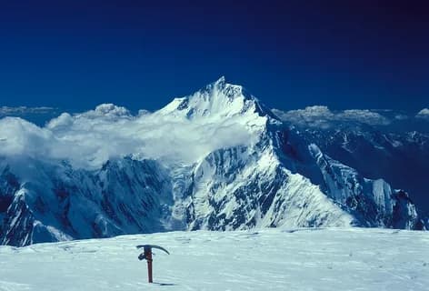 An ice axe planted in the snow in front of the Rakaposhi summit rising above a sea of cloud