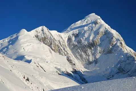 The snow-covered summit pyramid of Spantik in a deep blue sky above snow slopes
