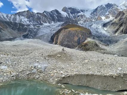 A lone figure on the boulder-covered snout of the Masherbrum glacier below its ice and snow peaks