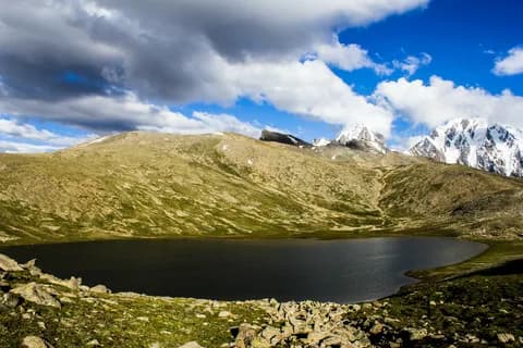 Rush Lake, a dark tarn on a green and gold alpine plateau under a dramatic cloud sky