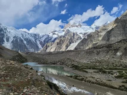 A grey glacial lake among moraine flats below a broad snow-covered mountain face