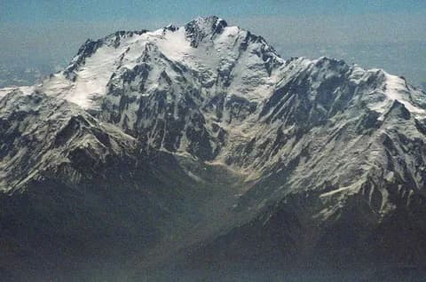 The snow-covered summit massif of Nanga Parbat rising above dark forested foothills