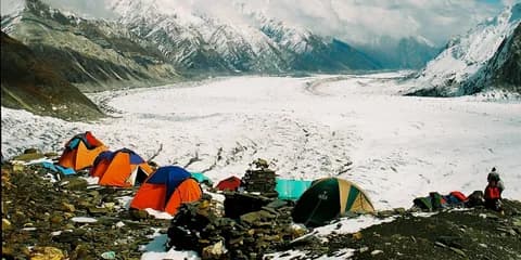 Orange and blue tents on a rocky ridge above the white expanse of the Spantik glacier basin
