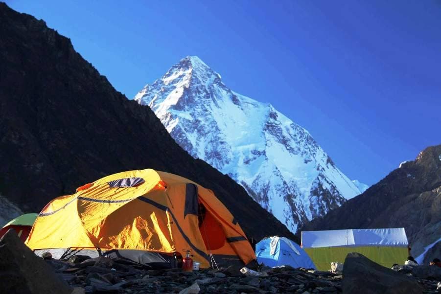 K2 rising above orange and blue tents at a rocky base camp
