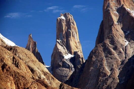 Sheer granite spires of the Trango Towers rising above brown Karakoram ridges against a deep blue sky