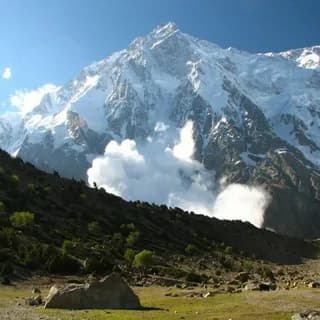 Massive snow-covered mountain face rising above a green valley with cloud drifting across the slopes