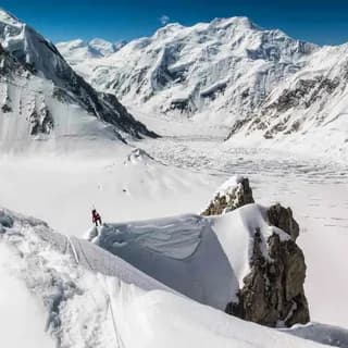 Climber standing on a snow ridge above a wide glacier basin ringed by distant peaks