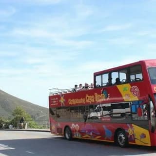 Red open-top sightseeing bus on a coastal road below green hills
