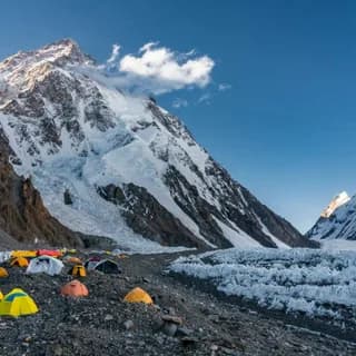 Colourful tents of a base camp on stony ground beside a glacier below a snow-covered peak