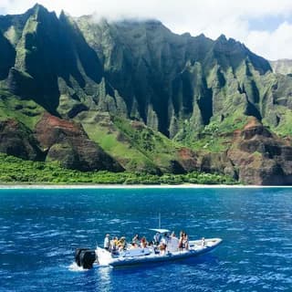 Small tour boat on turquoise water beneath towering green sea cliffs