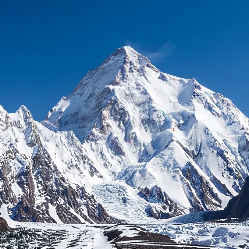 Snow-covered pyramid peak rising above the glacier tongue of a high Karakoram valley under a clear blue sky