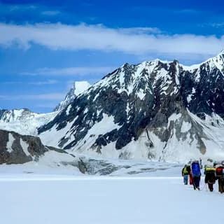 Group of trekkers crossing a wide snowfield beneath rocky peaks