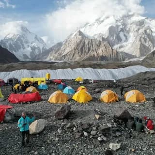 Large expedition camp of colourful tents on rocky ground below snow-covered peaks