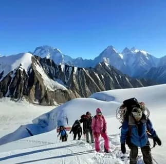 Roped climbers in colourful gear crossing a glacier below snow peaks
