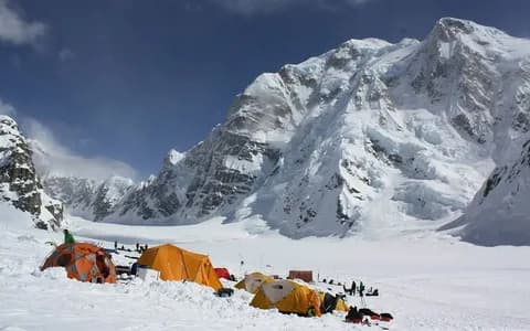 Expedition tents on the glacier below a vast snow-covered mountain face