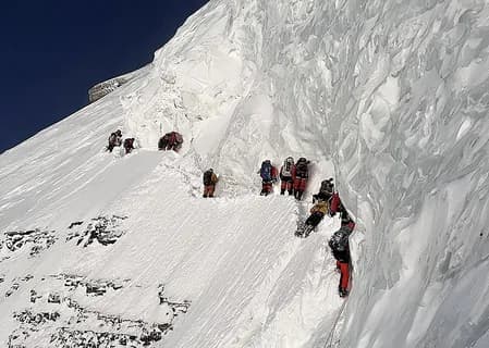 Roped climbers ascending a steep snow face past a high-altitude camp