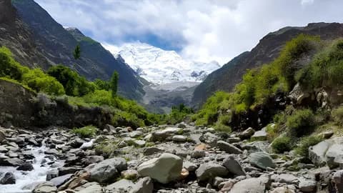 Green valley with a rocky riverbed leading towards a glacier