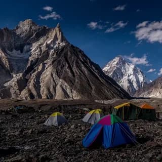 Tents at a stony base camp beneath snow-capped peaks