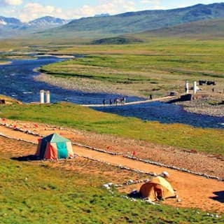Green alpine plain with a stream, footbridge and camp tents