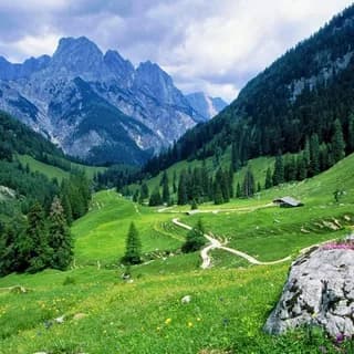 Lush green valley with winding paths beneath rugged peaks