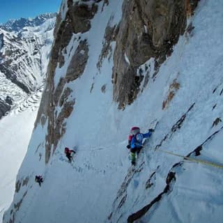 Two climbers ascending a steep snow-and-rock face on a fixed rope