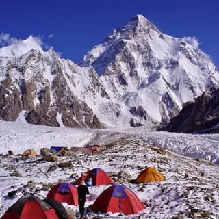 Colourful expedition tents pitched on rocky moraine below a snow-covered peak