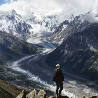 Trekker looking out over a broad glacier valley from a rocky viewpoint